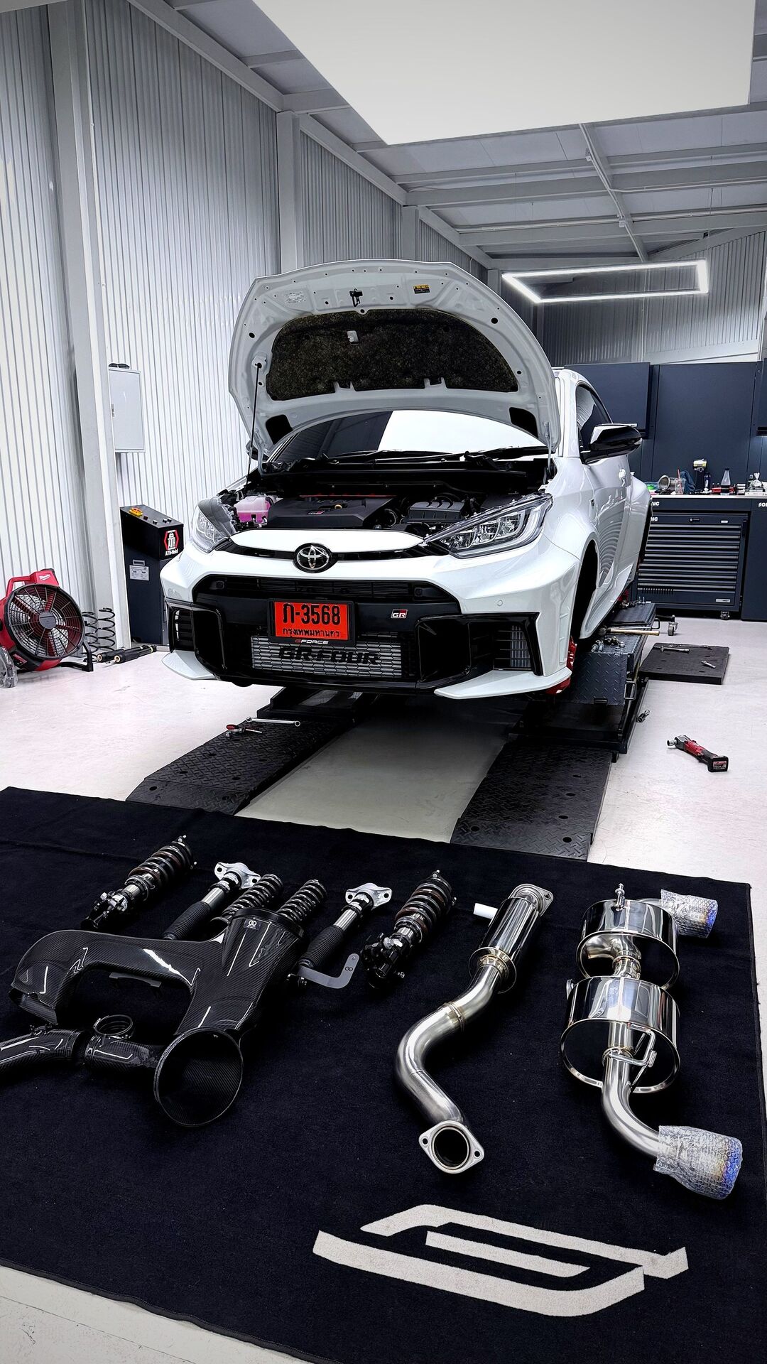 GR Yaris parts flatlay — NeoTech coilover, HKS Super Turbo Muffler laid out on G-FORCE mat