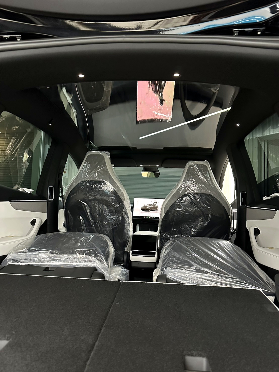 หลังคากระจก Tesla Model Y ก่อนติดม่านหลังคาไฟฟ้า เห็นเพดานโชว์รูมสะท้อนบนกระจก